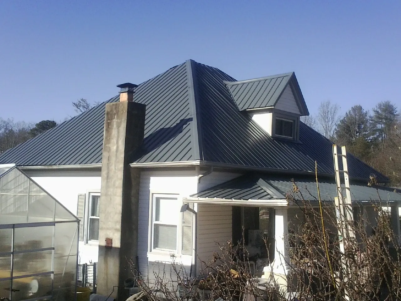 Dark blue standing seam metal roof on a white farmhouse with dormer — Slate & Tile Roof Repair by Roofing Brothers in Lansing