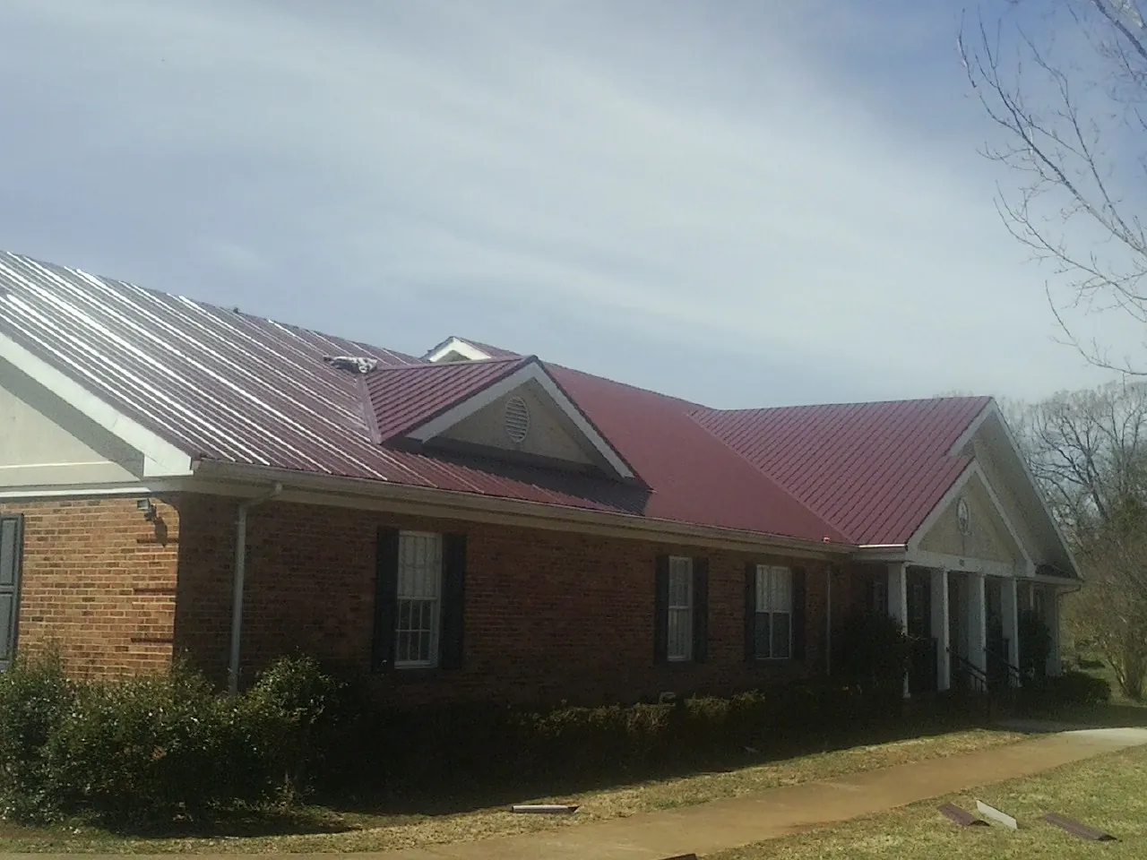 Red metal roof with gabled entries on a long brick building, from a Hail Damage Roof Repair job in Lansing