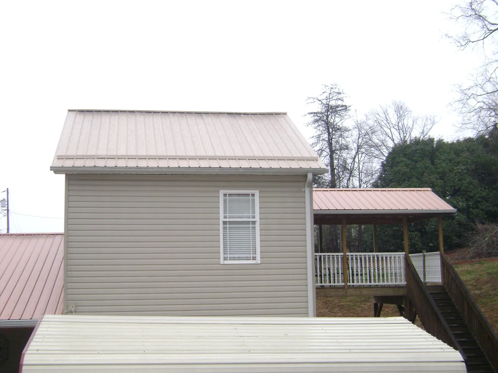 Tan metal roofs on a two story addition and attached porch, from a Roof Replacement job in Lansing
